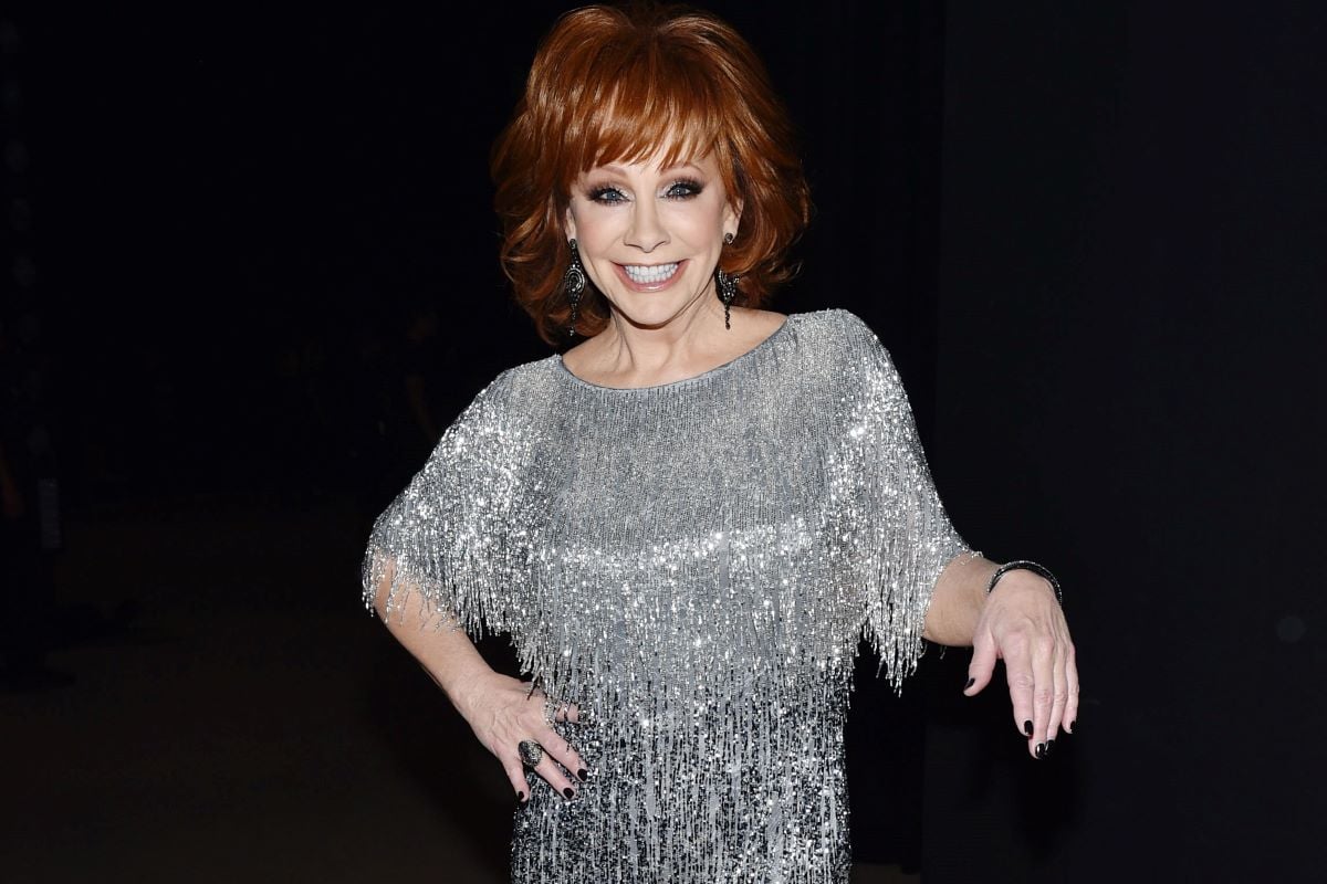 Reba McEntire in a silver fringe dress, holding one hand up and placing the other on her hip