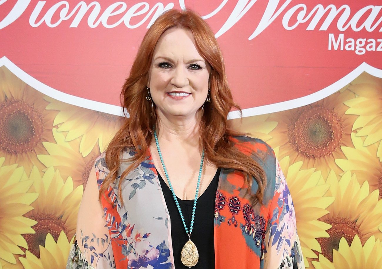 Ree Drummond smiles as she poses in front of a yellow sunflower sign that reads 'Pioneer Woman Magazine'