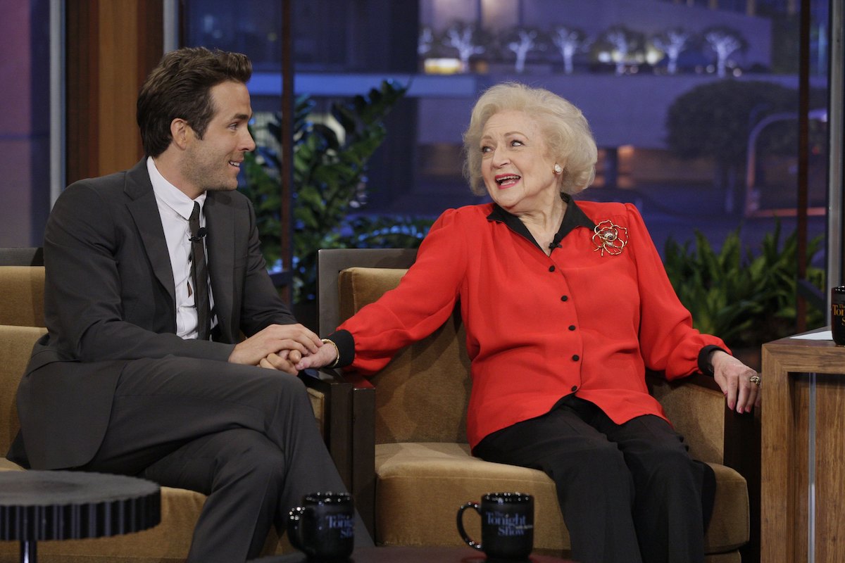 Ryan Reynolds and Betty White sit on a couch together and hold hands.