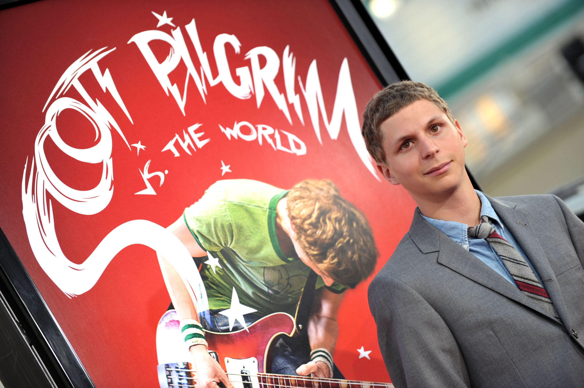 Michael Cera standing in front of a 'Scott Pilgrim vs. the World' poster at the premiere for the 2010 comics adaptation
