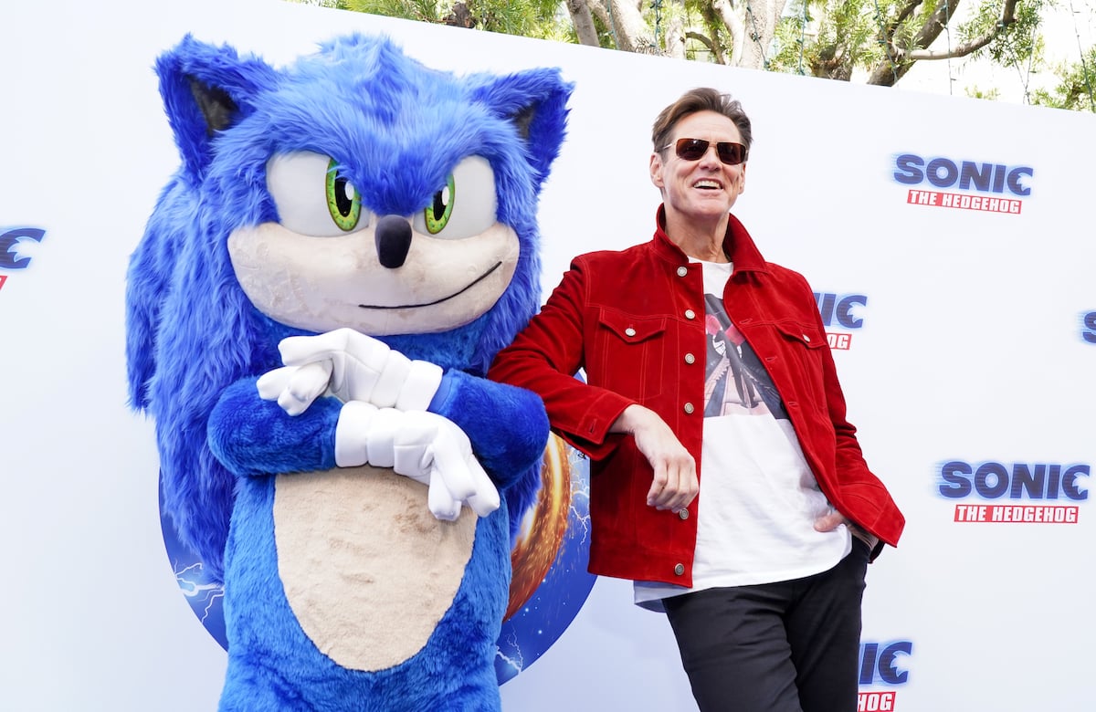 Jim Carrey wears a red jacket and poses next to a costumed Sonic the Hedgehog on the red carpet