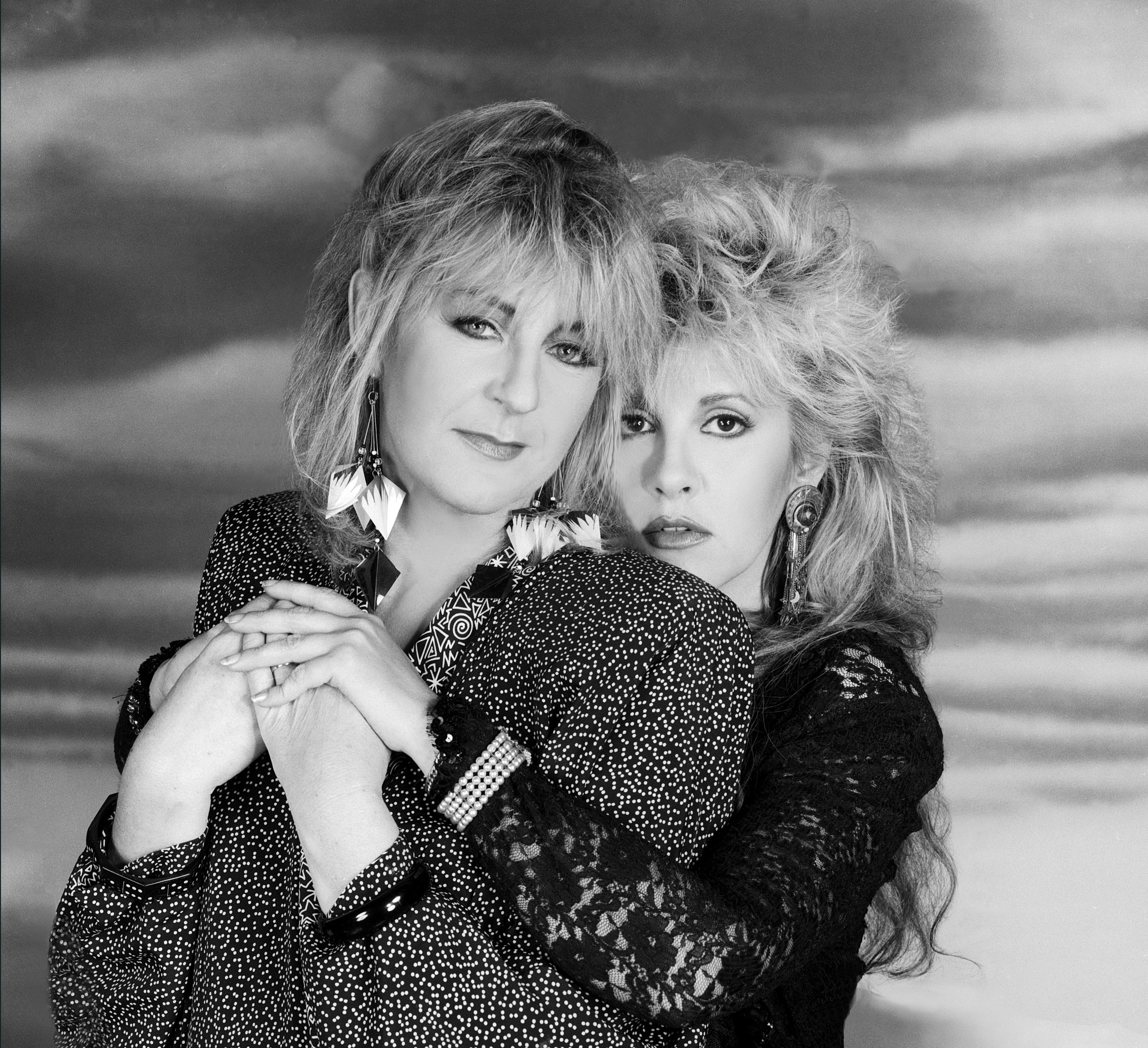 A black and white photo of Stevie Nicks standing behind Christine McVie and embracing her.
