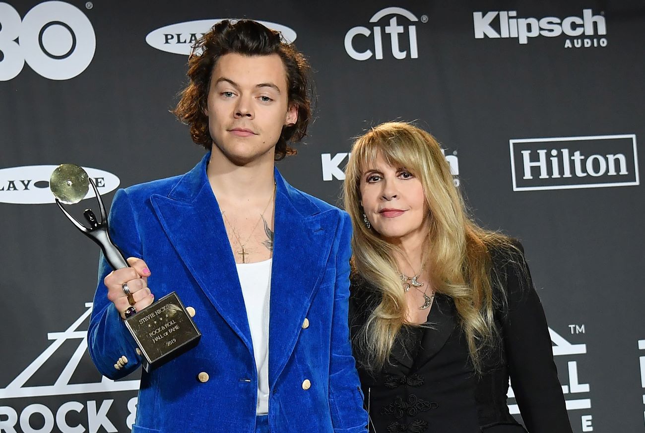 Harry Styles wears a blue suit and holds an award. Stevie Nicks stands next to him in a black dress.