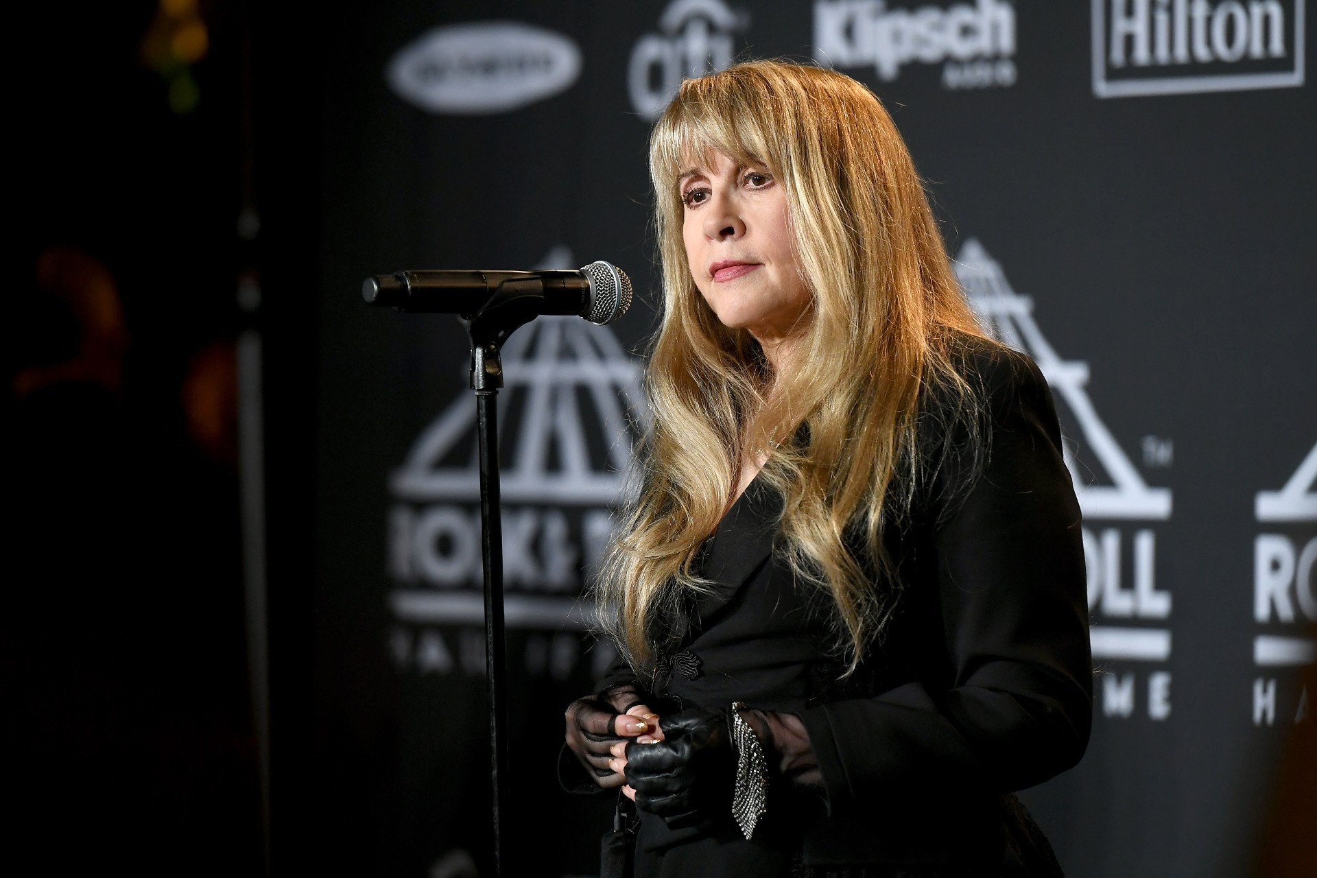 Stevie Nicks holds a microphone while performing in a black outfit.