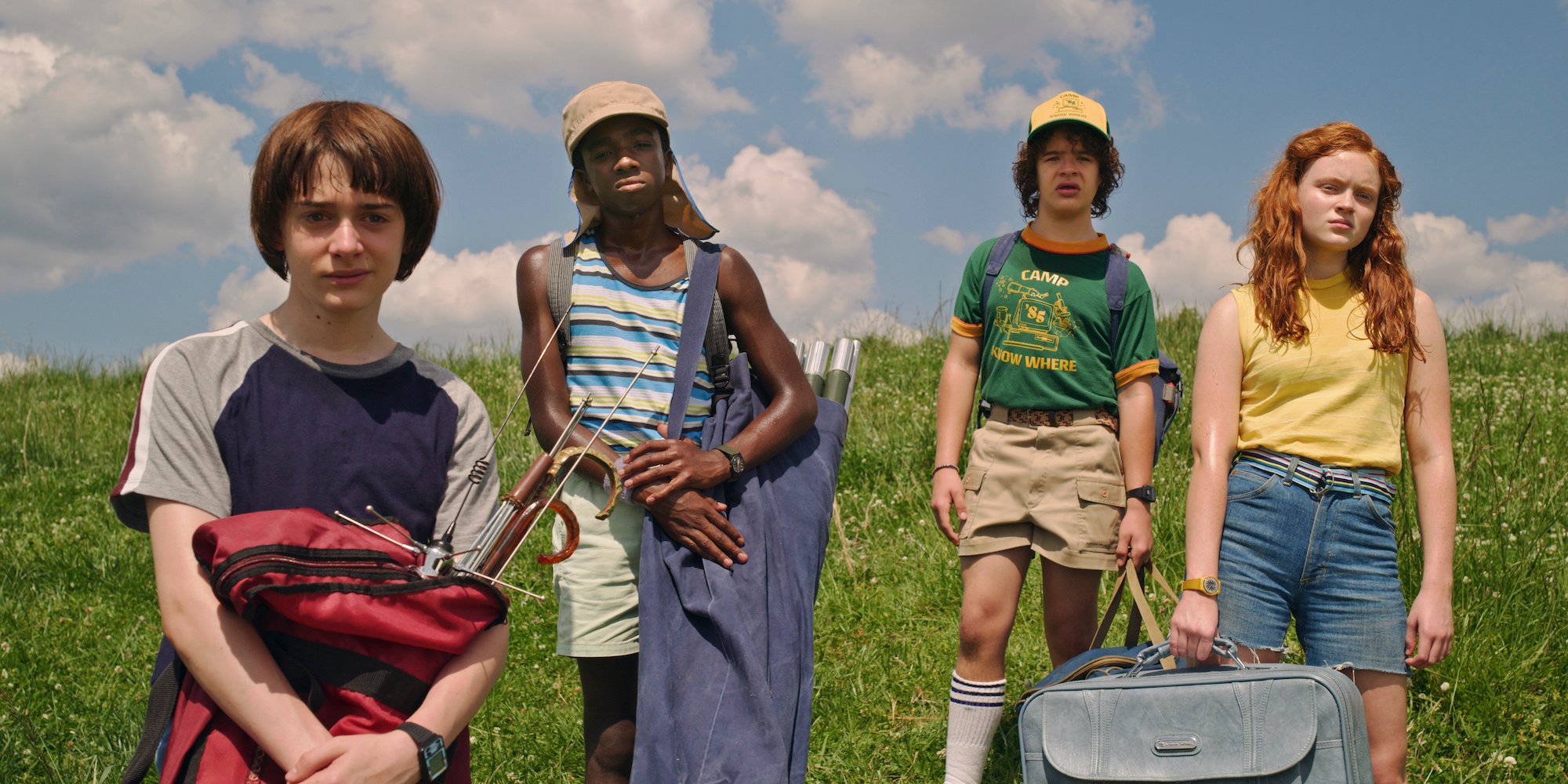 'Stranger Things' Season 3 production still of Will Byers, Lucas Sinclair, Dustin Henderson, and Max Mayfield standing in a field