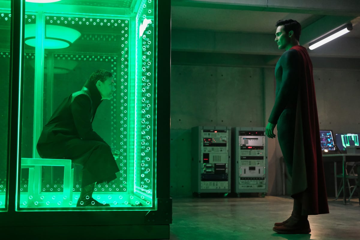 'Superman & Lois' Season 2 actors Adam Rayner and Tyler Hoechlin, in character as Tal-Rho and Superman, share a scene while Tal-Rho is in a containment cell and Superman is talking to him outside of it. Tal-Rho wears a black cloak. Superman wears his red, blue, and yellow costume.