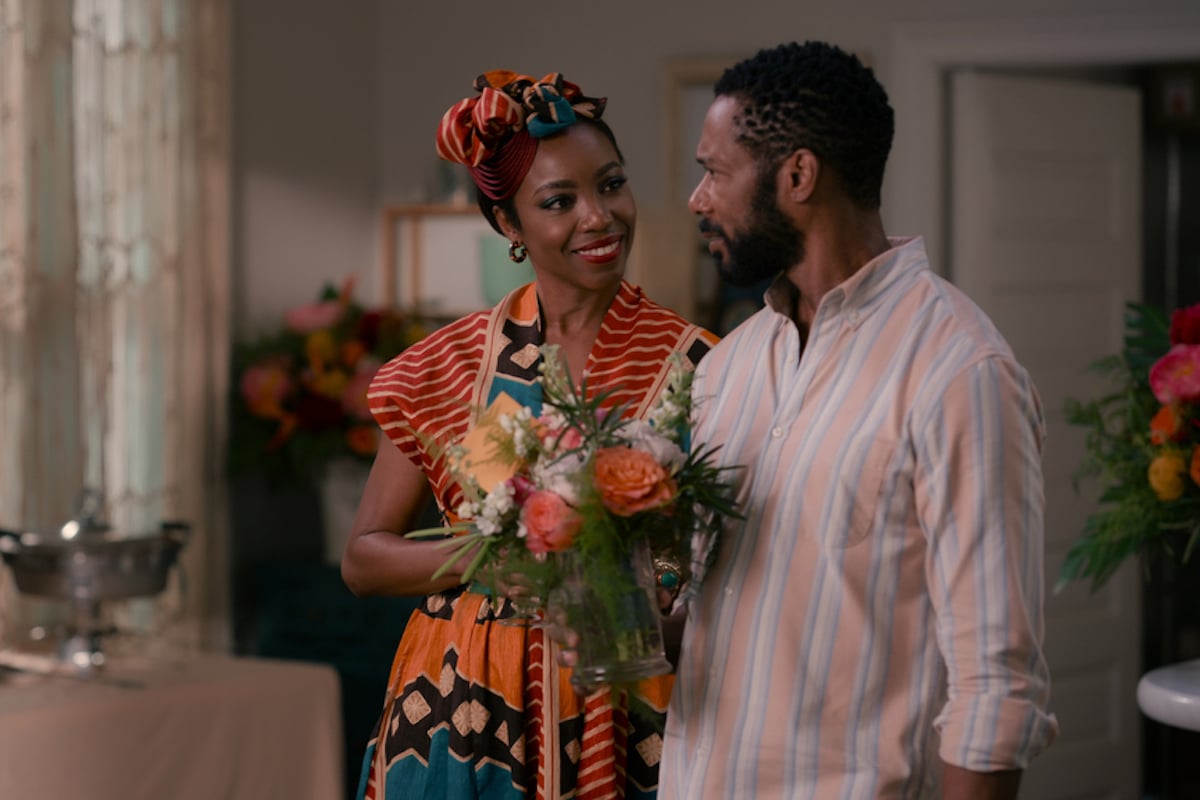 Helen, wearing a head scarf, standing next to Erik, holding a vase of flowers in 'Sweet Magnolias' Season 2