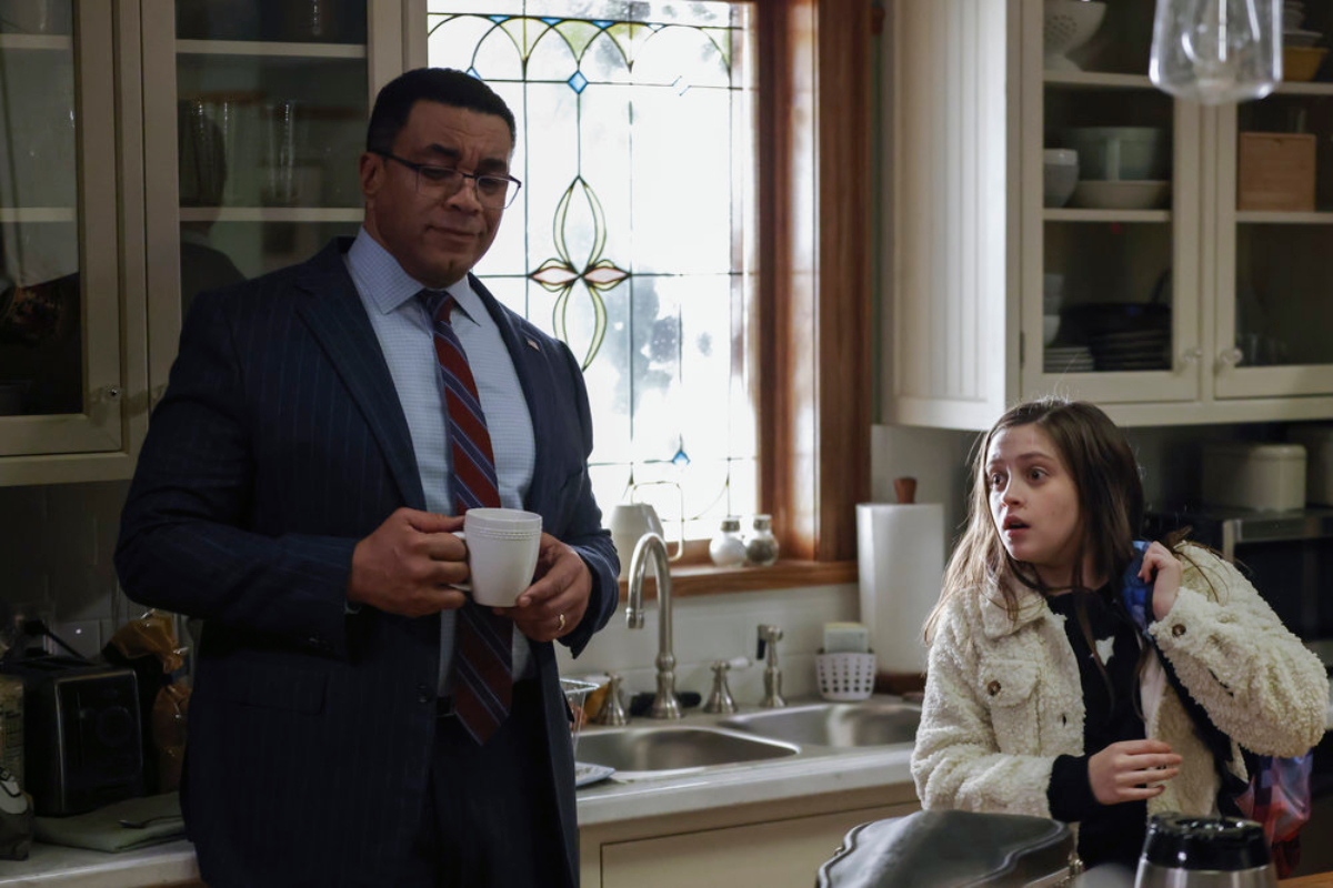 Harry Lennix as Harold Cooper and Sami Bray as Agnes in The Blacklist Season 9. Cooper stands in the kitchen holding a coffee mug and Agnes has her backpack over her shoulder.