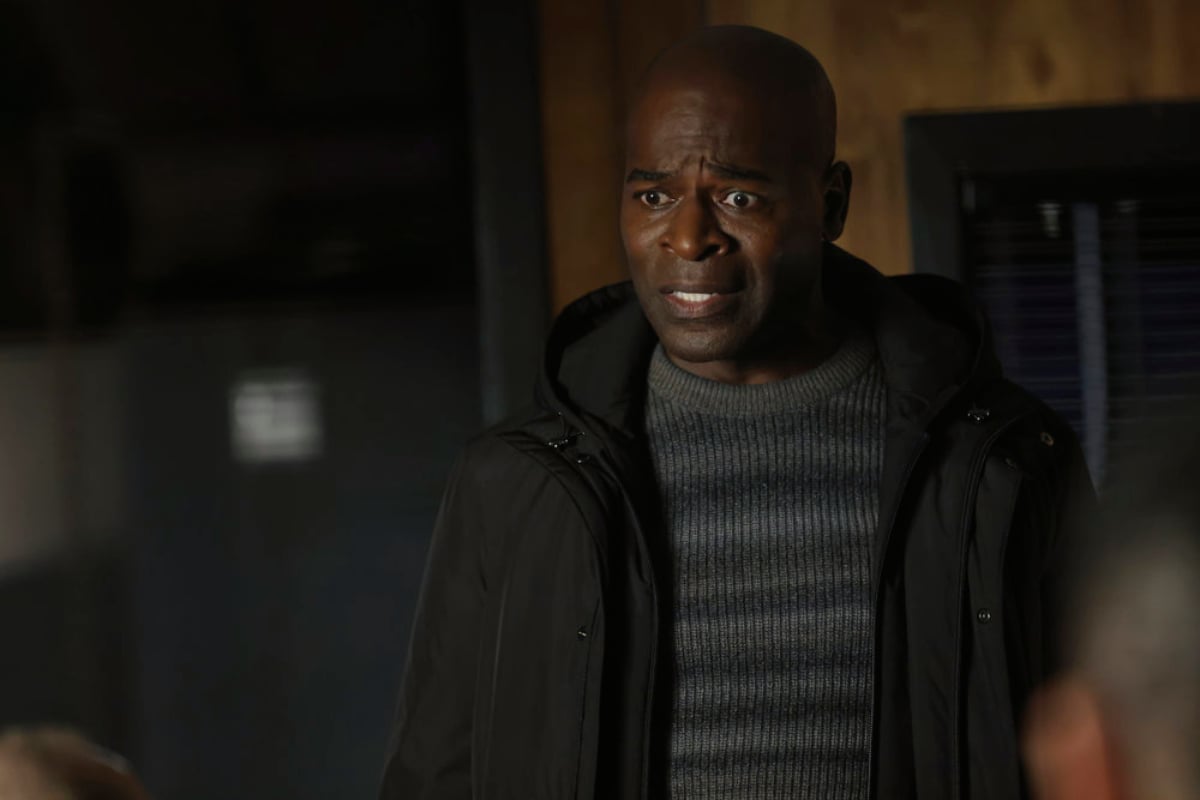 Hisham Tawfiq as Dembe Zuma in The Blacklist Season 9. Dembe wears a striped sweater and black coat and looks distressed.