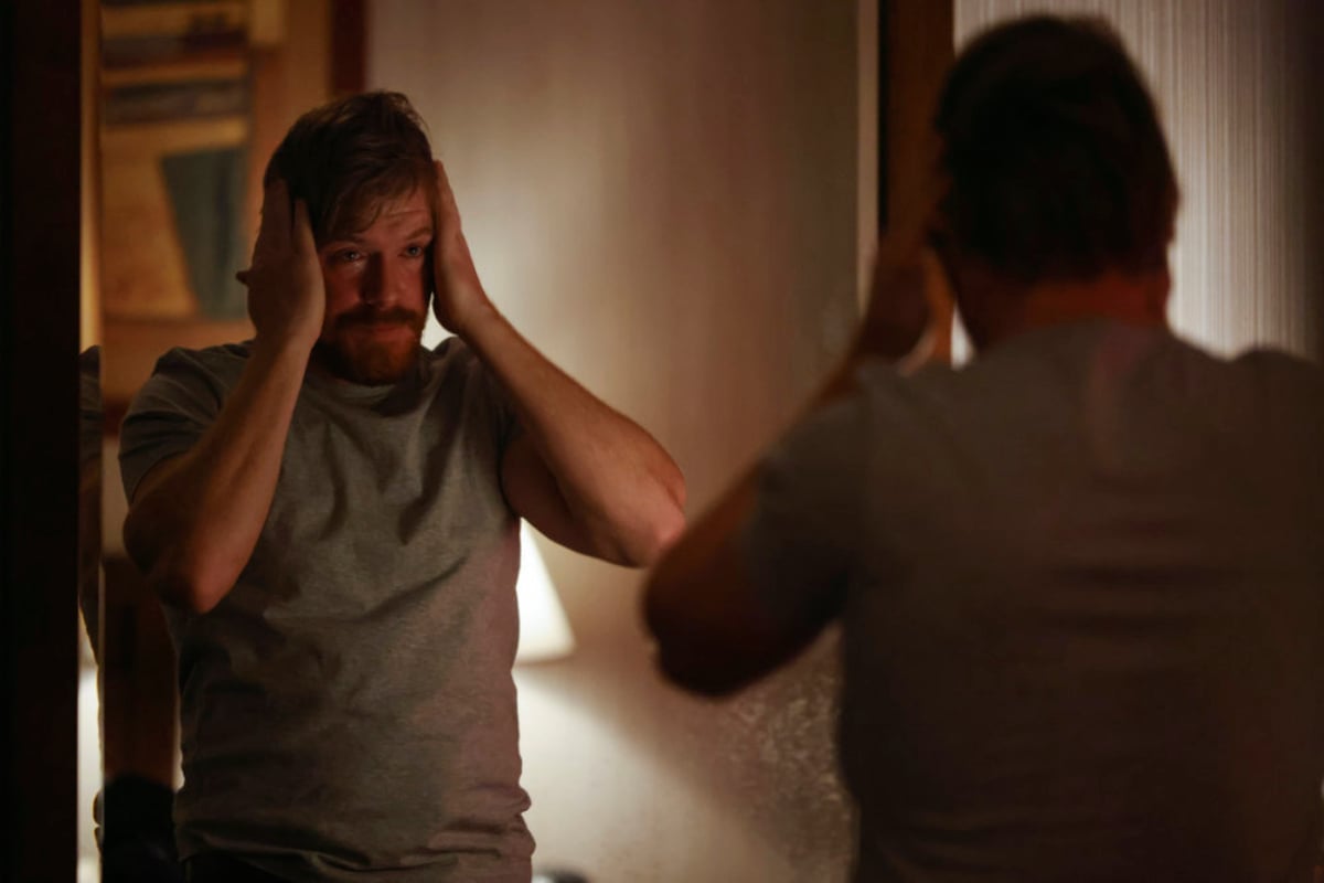 Diego Klattenhoff as Donald Ressler in The Blacklist Season 9. A disheveled-looking Ressler stares at his reflection with his hands on both sides of his head.