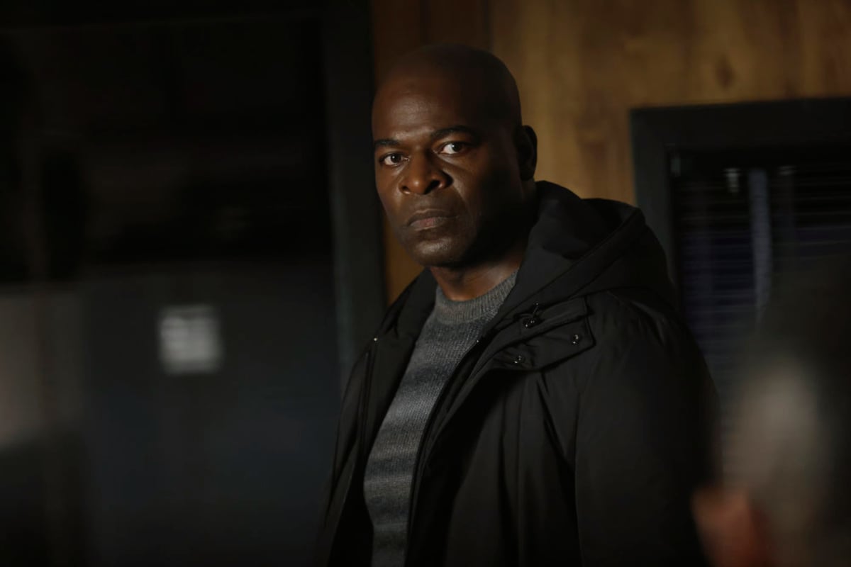 Hisham Tawfiq as Dembe Zuma in The Blacklist Season 9. Dembe wears a striped sweater and black jacket.