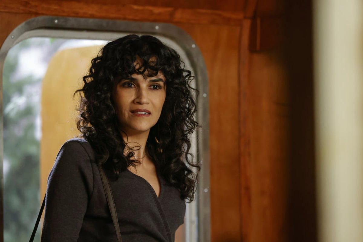 Karina Arroyave as Mierce Xiu in The Blacklist Season 9. Mierce stands in the doorway with a bag over her arm.