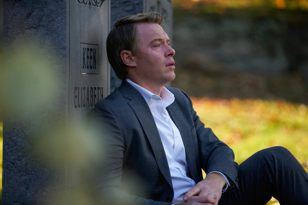 Diego Klattenhoff as Donald Ressler in The Blacklist Season 9. A teary-eyed Ressler sits with his back to LIz's tombstone.