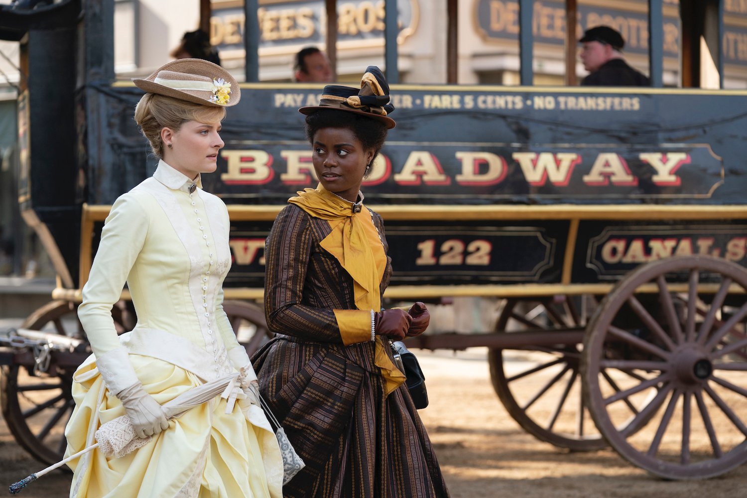 A white woman and a Black woman, both in 19th century dress, standing in front of an omnibus in HBO's 'The Gilded Age'