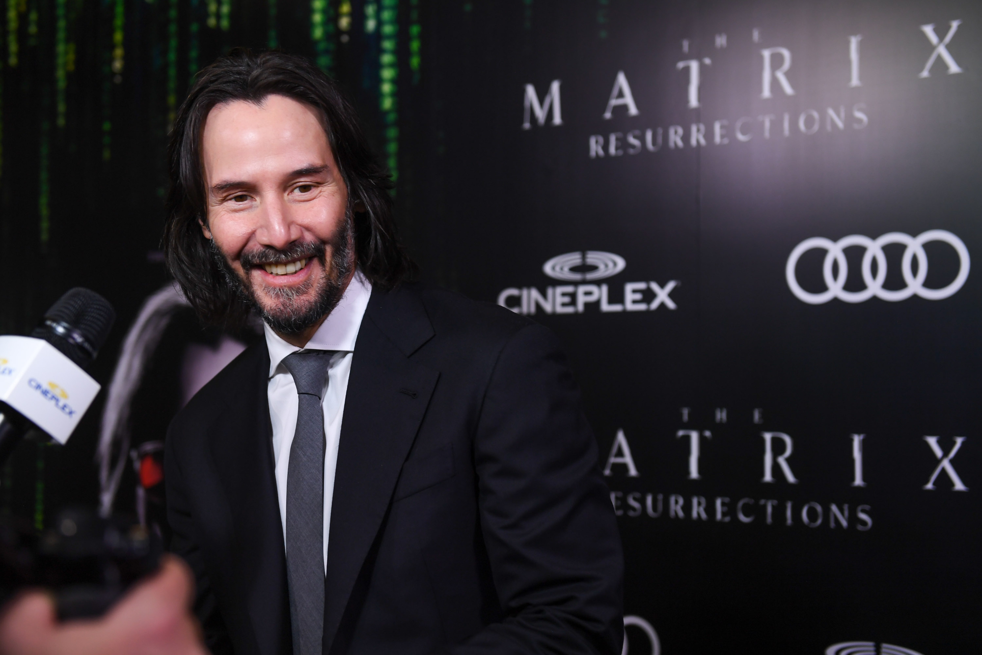 'The Matrix Resurrections' Keanu Reeves smiling in front of a step and repeat