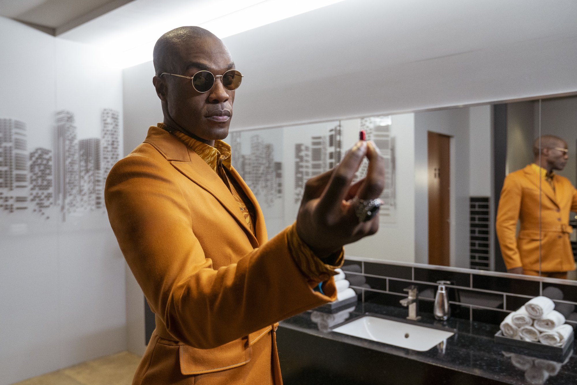 'The Matrix Resurrections' Yahya Abdul-Mateen II as Morpheus wearing a yellow suit holding a red pill in a bathroom