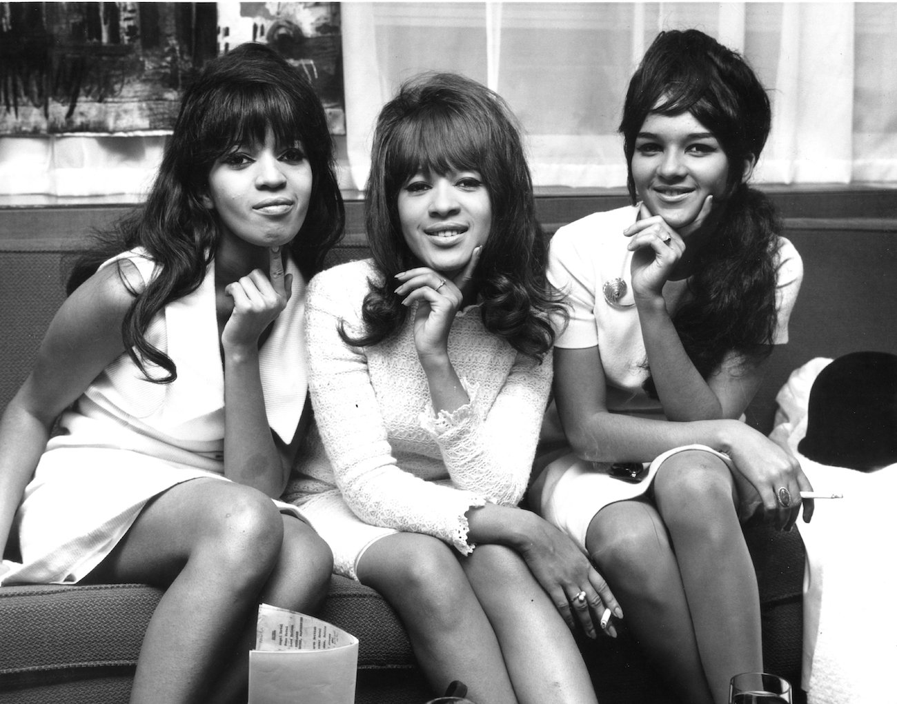 The Ronettes, Estelle Bennett, Ronnie Spector, and Nedra Talley posing for a photo wearing matching white outfits in 1964.