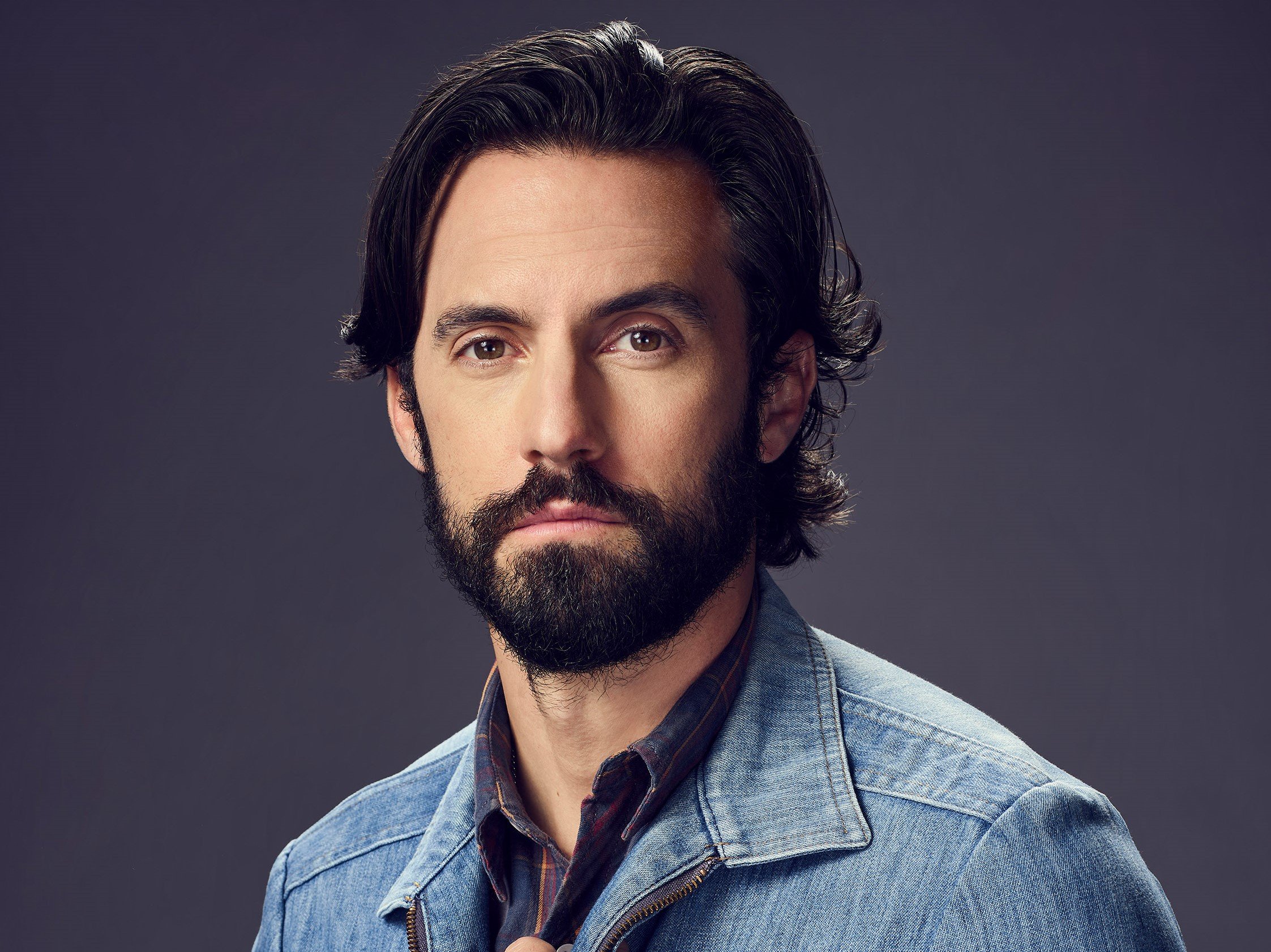 'This Is Us' star Milo Ventimiglia poses as Jack Pearson for promotional pictures for season 6. Ventimiglia wears a denim jacket over a dark plaid shirt.