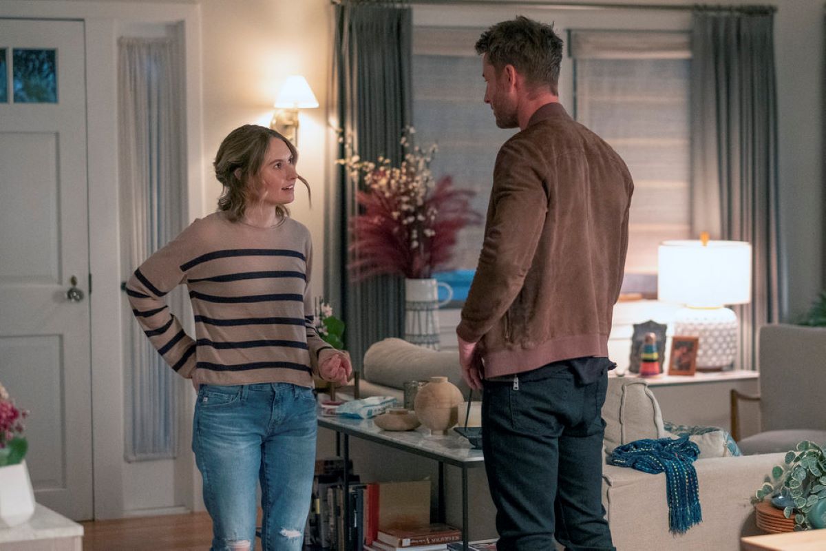 'This Is Us' Season 6 stars Caitlin Thompson and Justin Hartley, in character as Madison and Kevin, have a conversation in Madison's house. Madison wears a tan sweater with black horizontal stripes and jeans. Kevin wears a brown jacket and black pants.