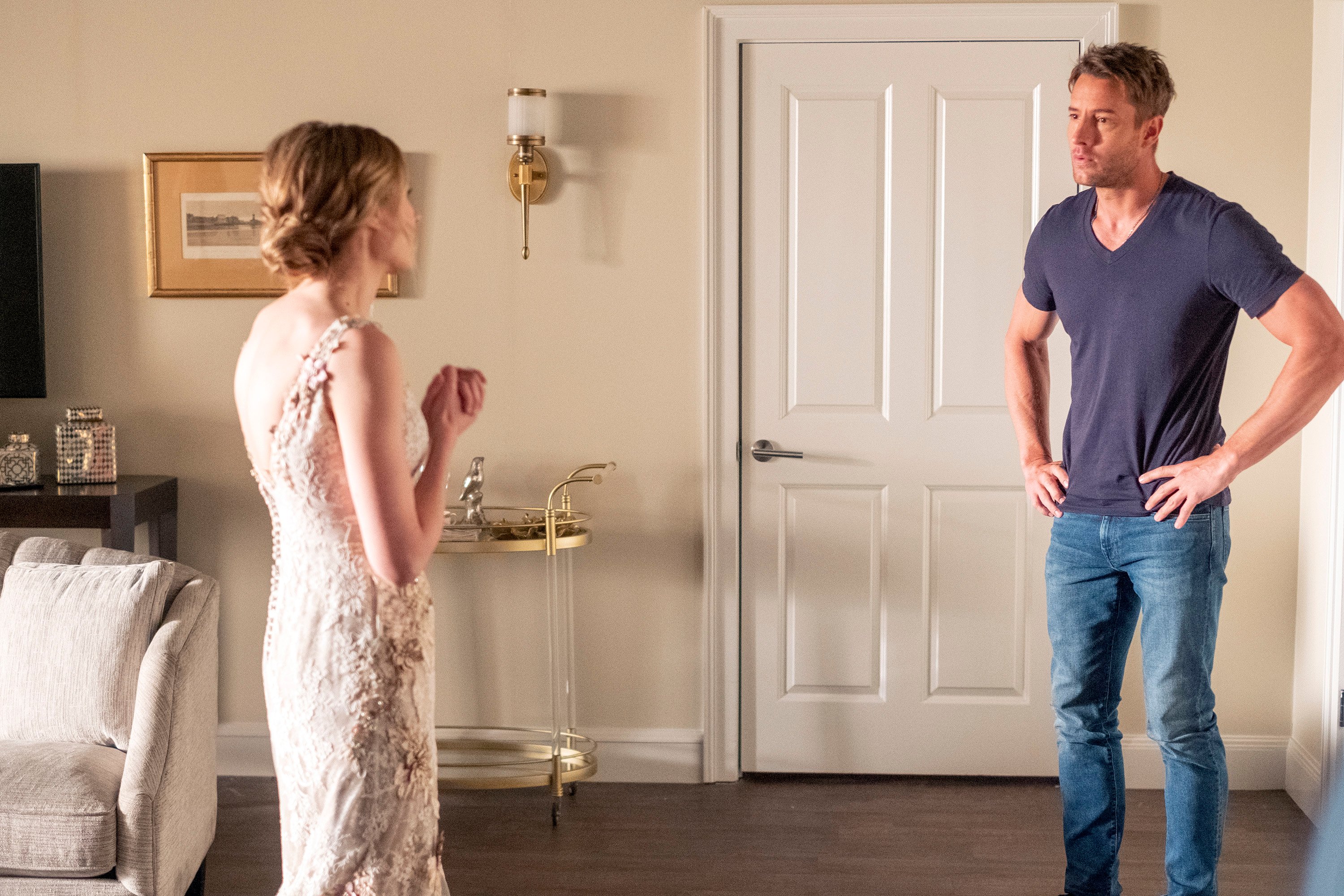 'This Is Us' Season 6 Episode 1 stars Caitlin Thompson and Justin Hartley, in character as Madison and Kevin, talk to one another. Madison wears a beaded white wedding dress. Kevin wears a dark blue t-shirt and jeans.