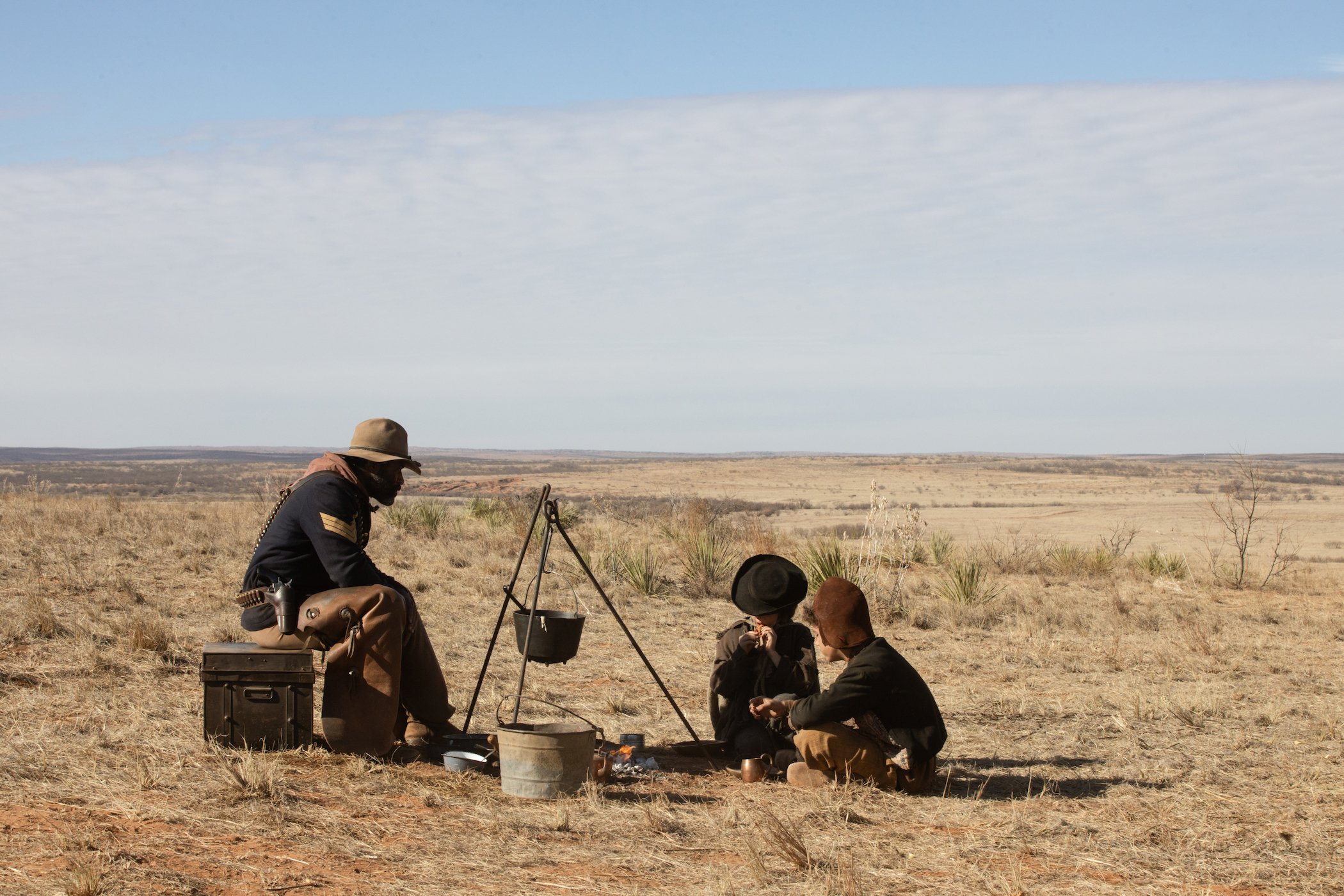 LaMonica Garrett sitting down with two others across from him in an open field in '1883'