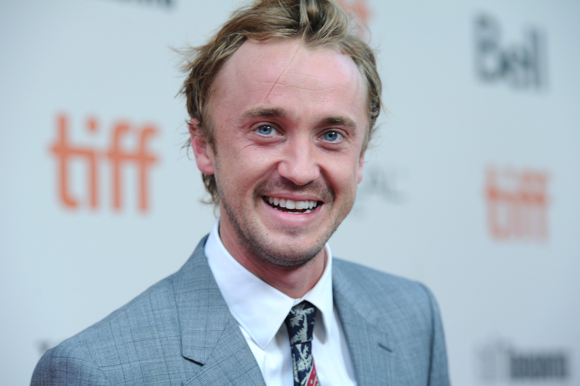 'Harry Potter' star Tom Felton. He's smiling and wearing a grey suit and white shirt.