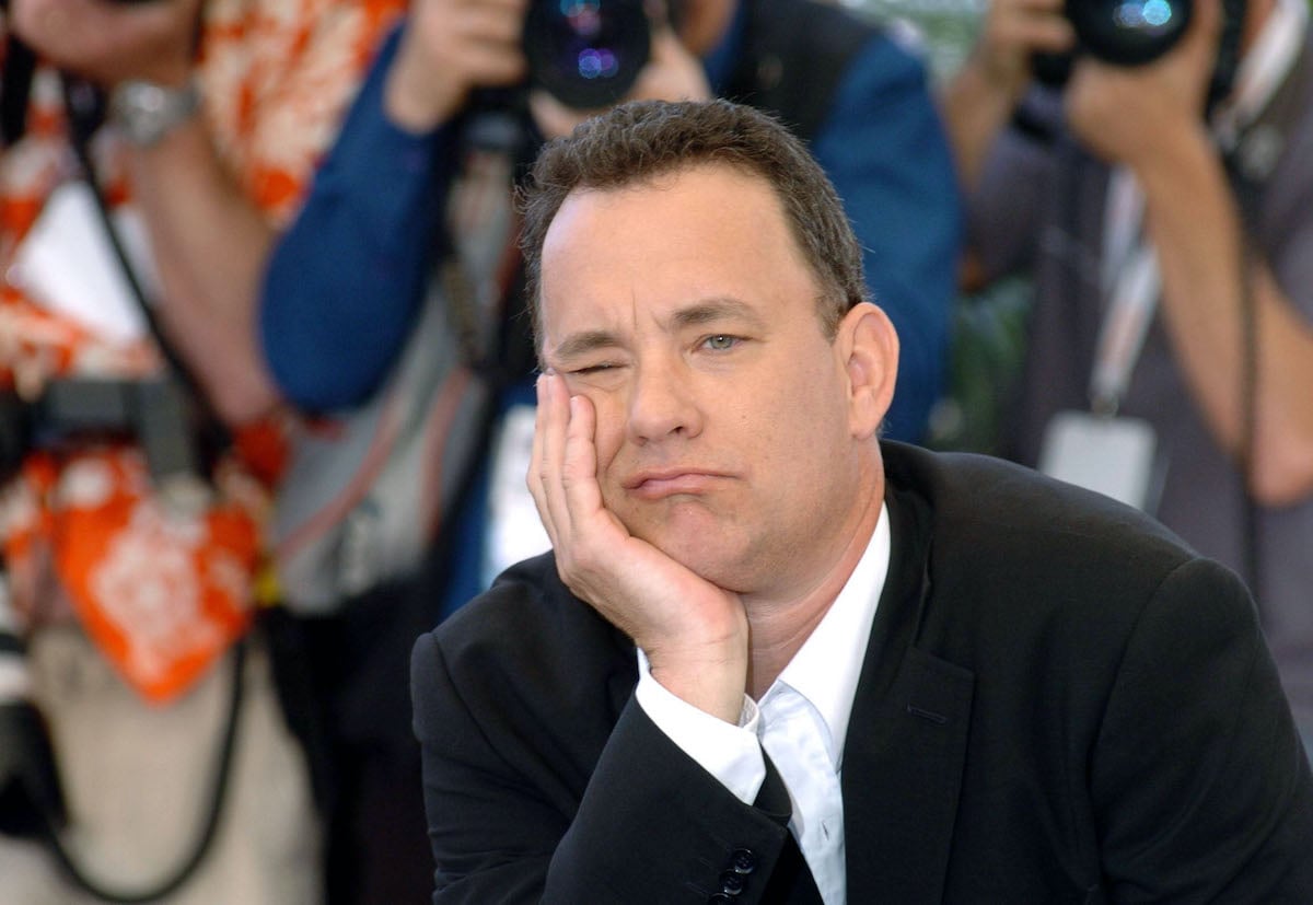 Tom Hanks leans his head on his hand while he wears a suit at a red carpet event