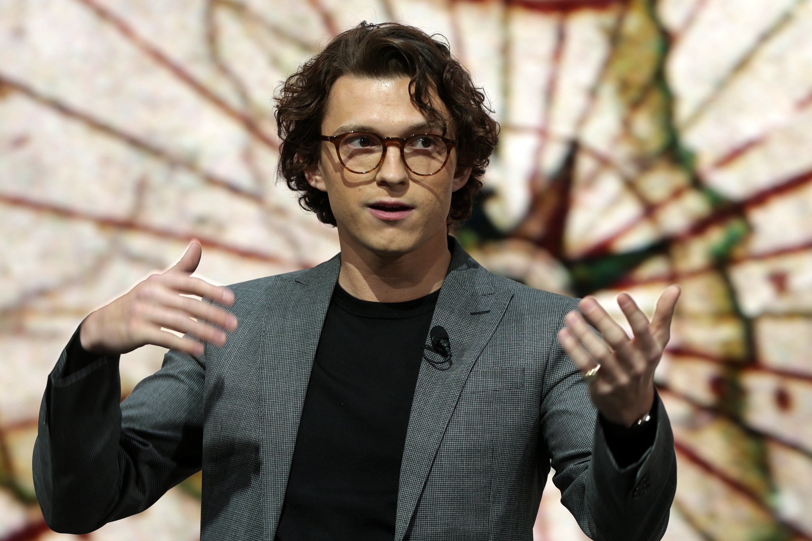 'Spider-Man: No Way Home' actor Tom Holland wears a gray blazer over a black t-shirt and glasses.