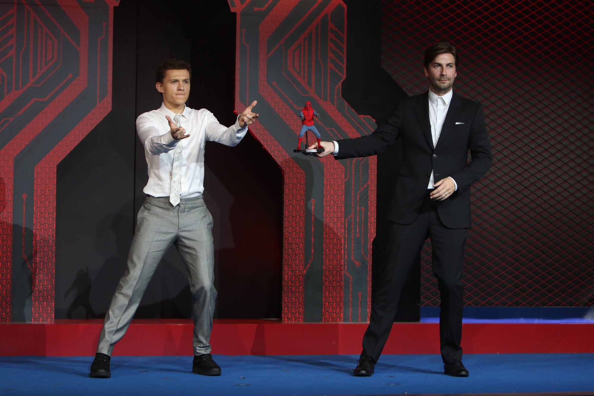 Spider-Man star Tom Holland and director Jon Watts. Holland is holding out his hands like Spider-Man, and Watts is holding a Spider-Man figure.
