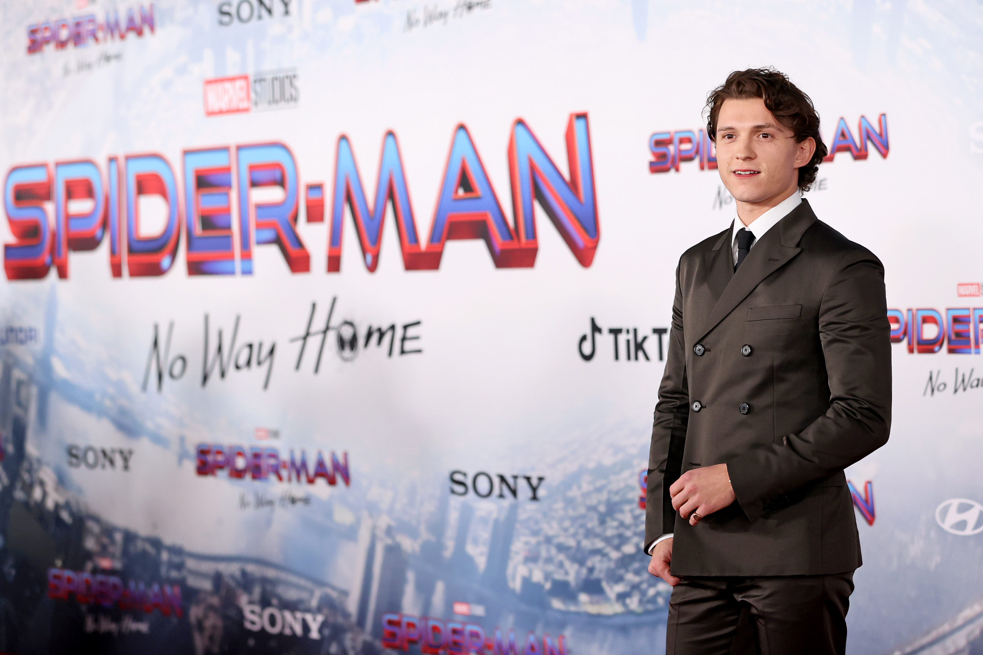 'Spider-Man: No Way Home' star Tom Holland wears a dark gray suit over a white button-up shirt and black tie.