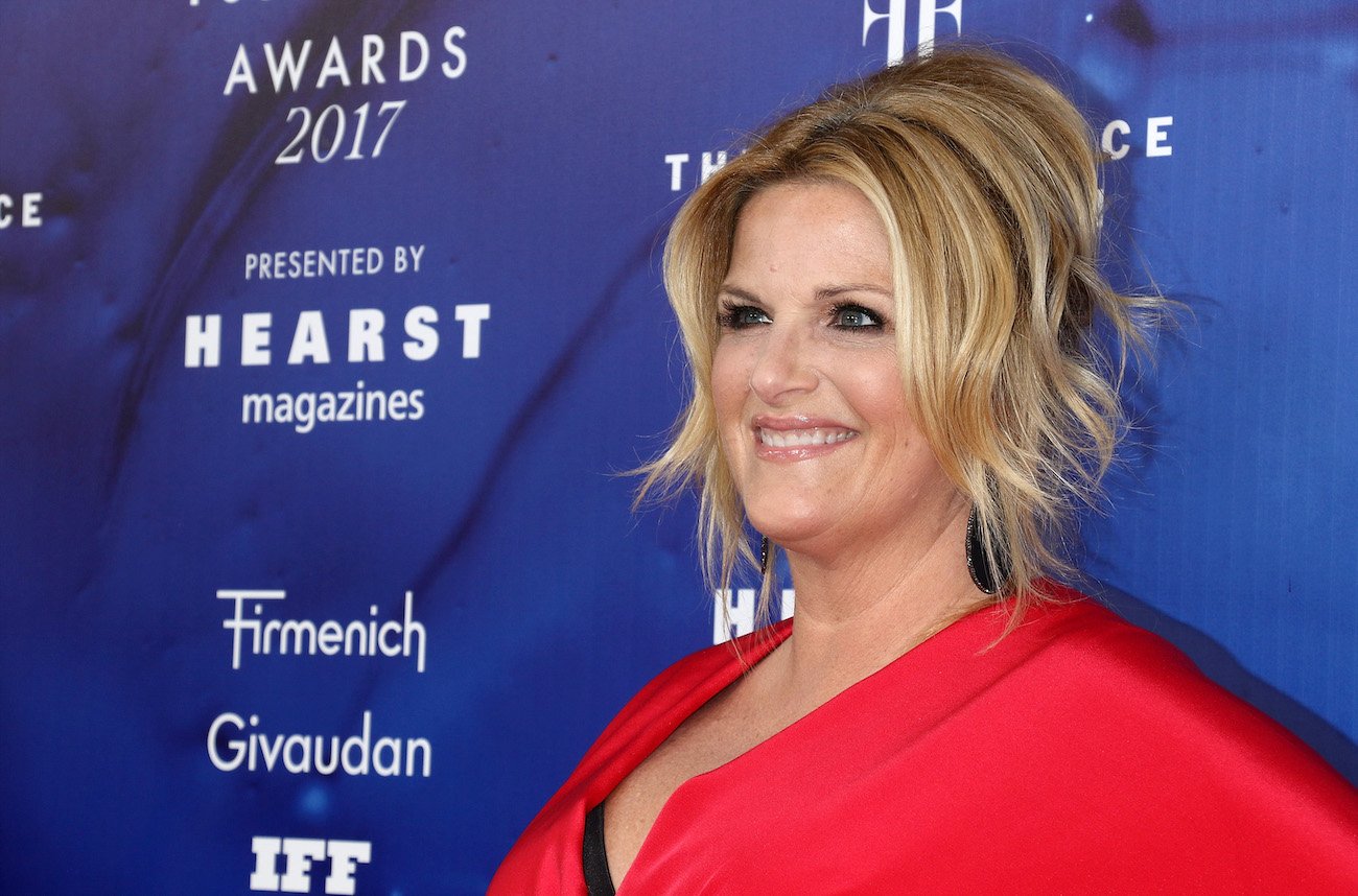 Trisha Yearwood smiles and she poses for cameras wearing a red dress