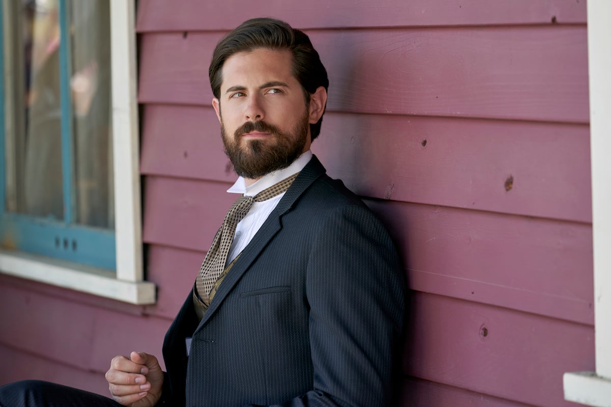 Chris McNally as Lucas, leaning against a red wall, in 'When Calls the Heart'