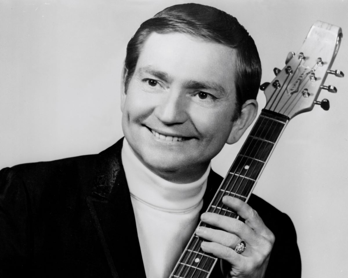 Willie Nelson with short hair, smiling and holding a guitar c. 1967