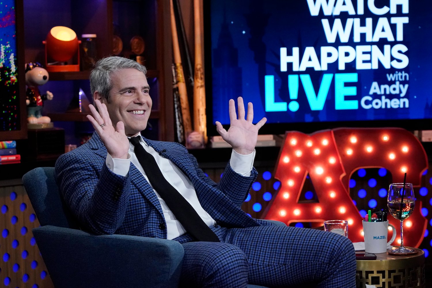 Andy Cohen sitting on the set of 'Watch What Happens Live', smiling, and holding up both of his arms