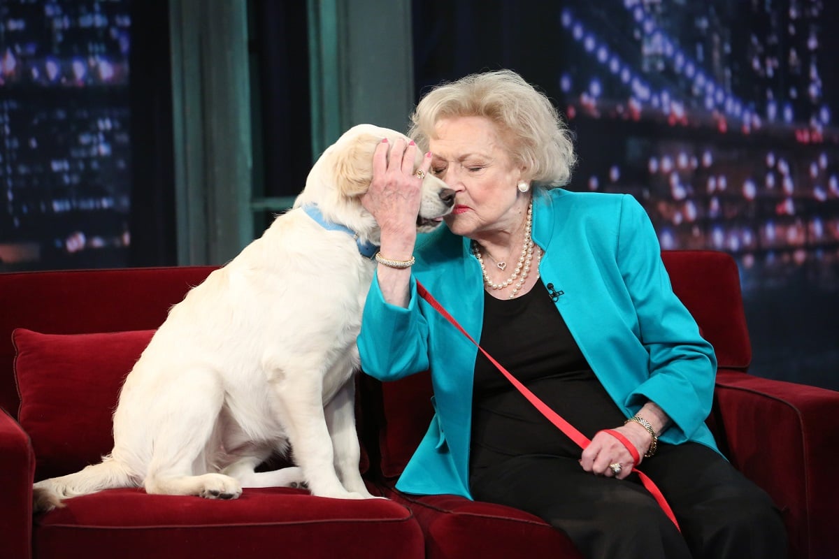 Betty White holds the leash of a dog while sitting on a couch.