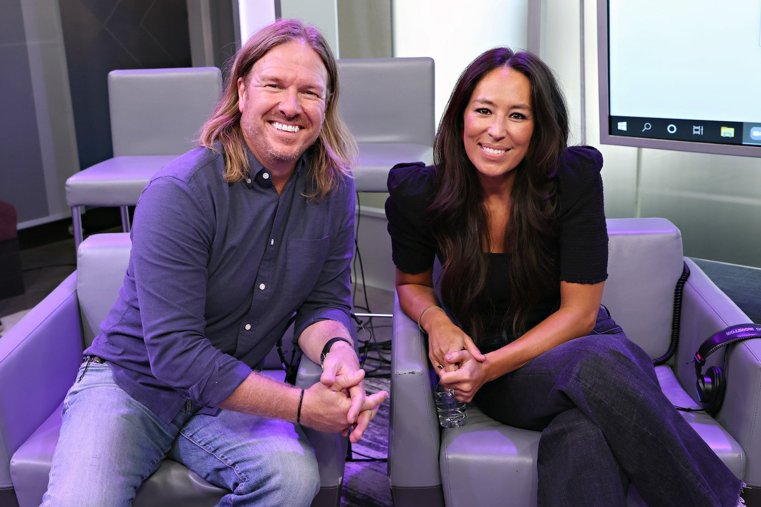 Chip and Joanna Gaines smile as they pose for the camera sitting in two chairs