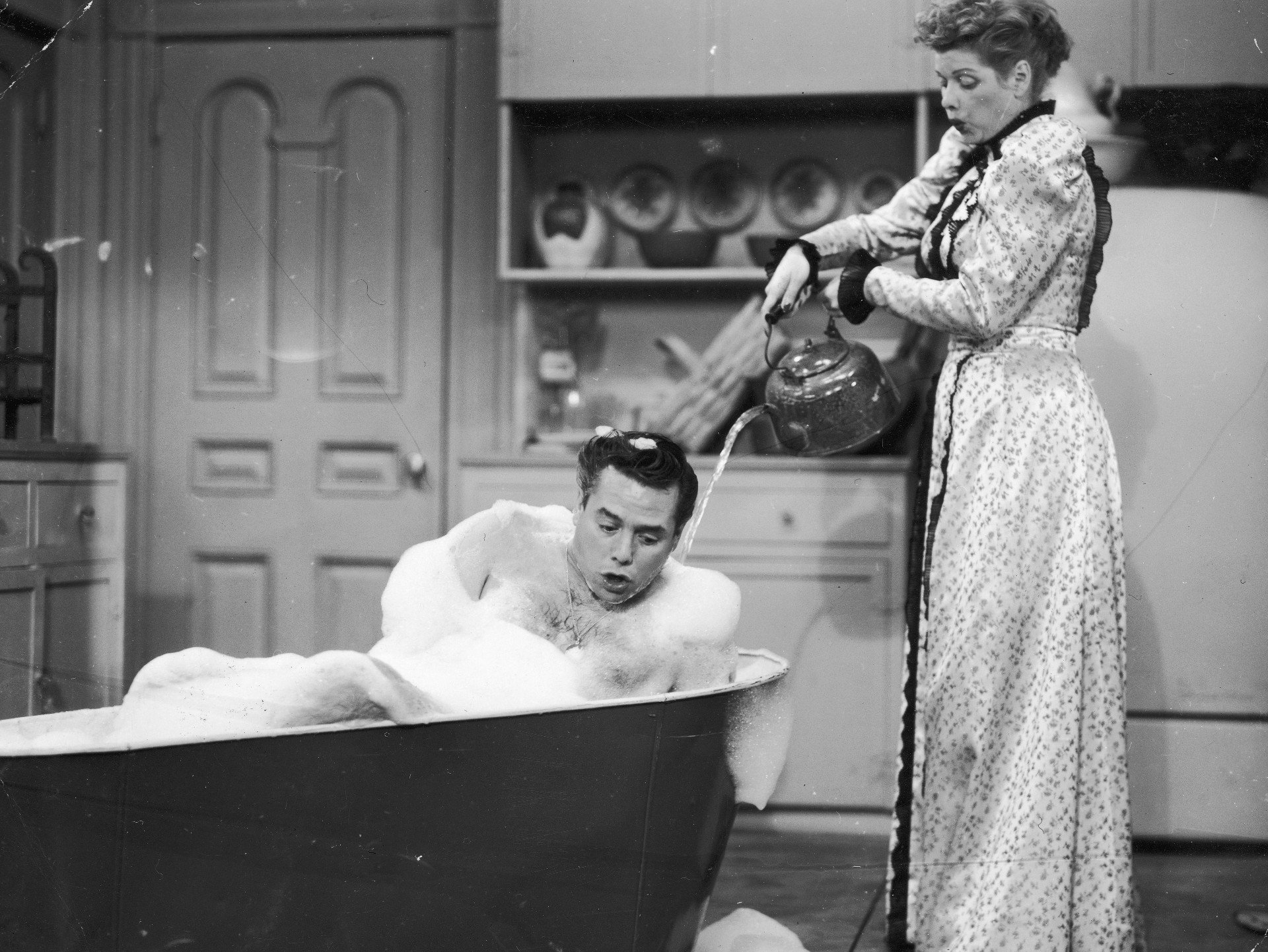 Desi Arnaz and Lucille Ball together as Lucille Ball pours a tea kettle with water over Desi Arnaz in a soapy bathtub