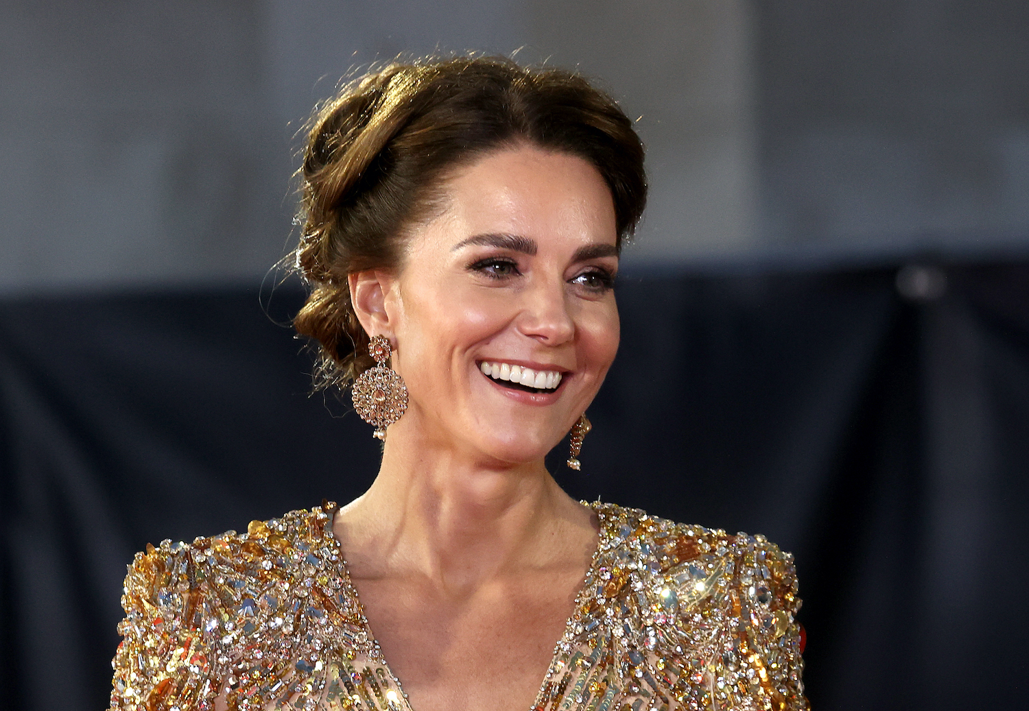 Kate Middleton wears a gold dress and smiles with her hair in an updo at the 'No Time To Die' premiere in 2021