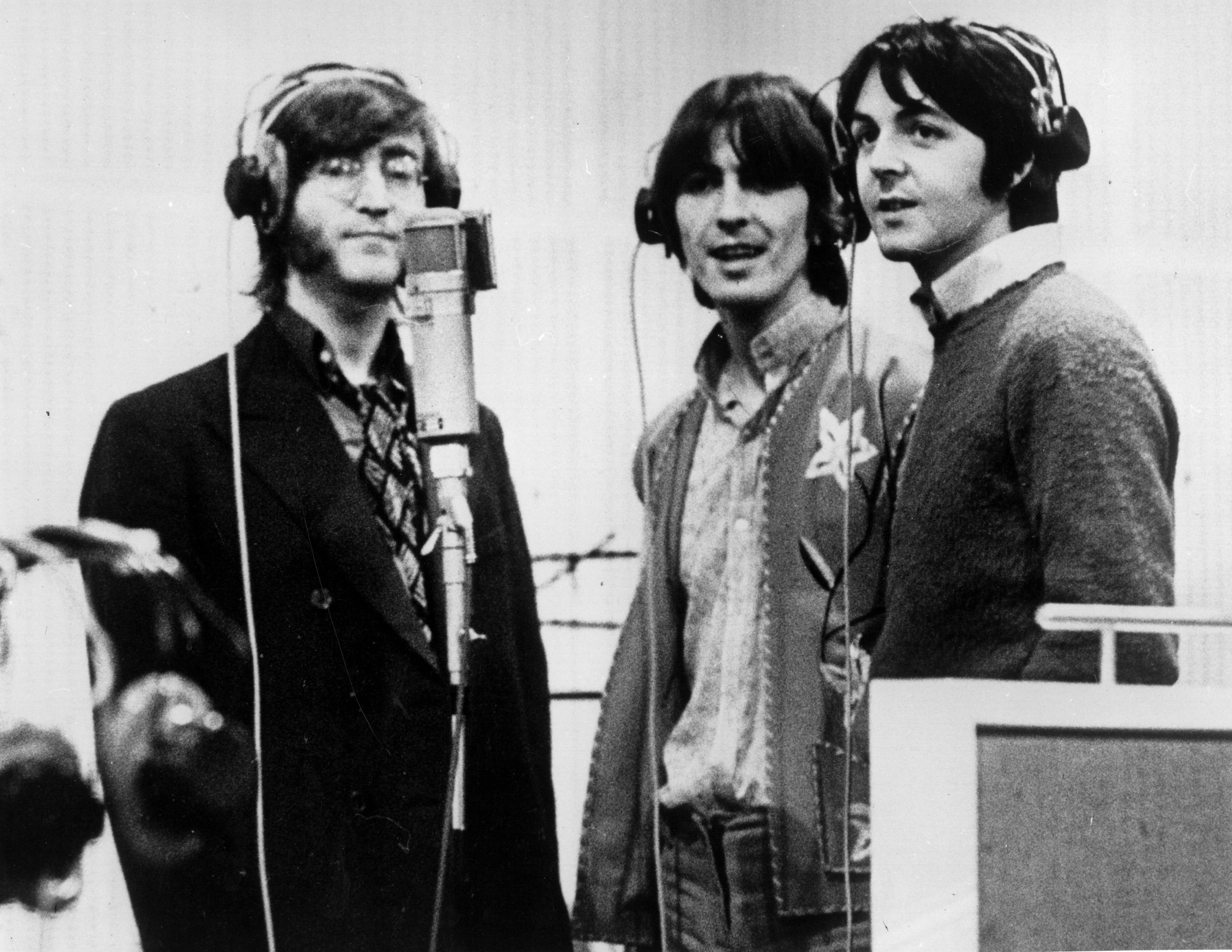 The Beatles' John Lennon, George Harrison, and Paul McCartney near a microphone recording lines for 'Yellow Submarine'