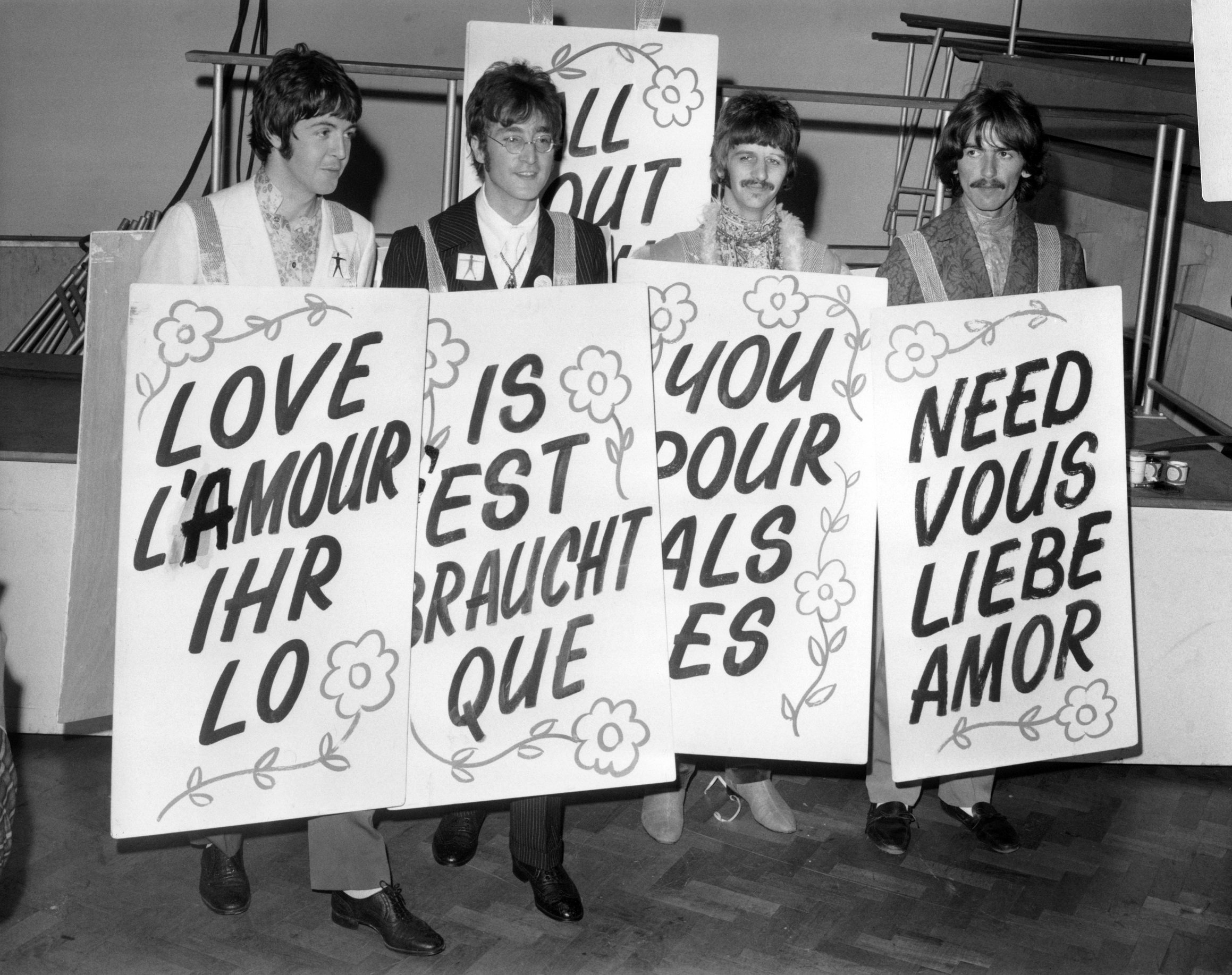 The Beatles' Paul McCartney, John Lennon, Ringo Starr and George Harrison with flowered signs that say 'All You Need Is Love' in multiple languages