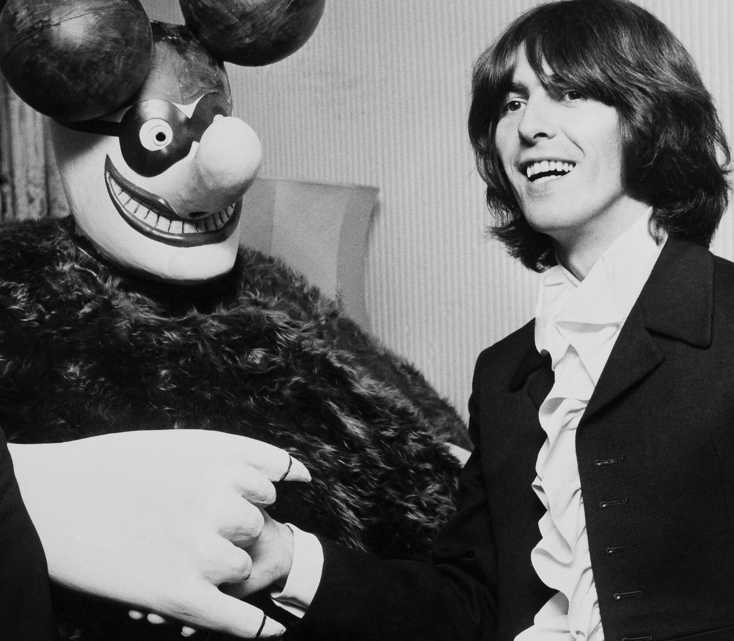 The Beatles' George Harrison wearing a suit and standing near someone dressed as a Blue Meanie from 'Yellow Submarine'