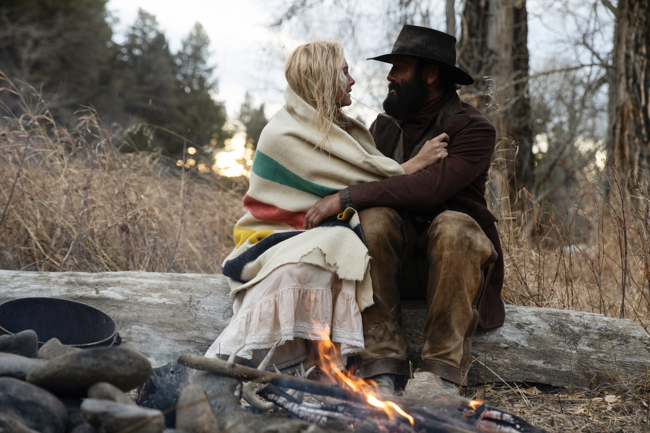 Isabel May as Elsa Dutton and Tim McGraw as James Dutton hugging each other while sitting on a log in '1883' episode 10