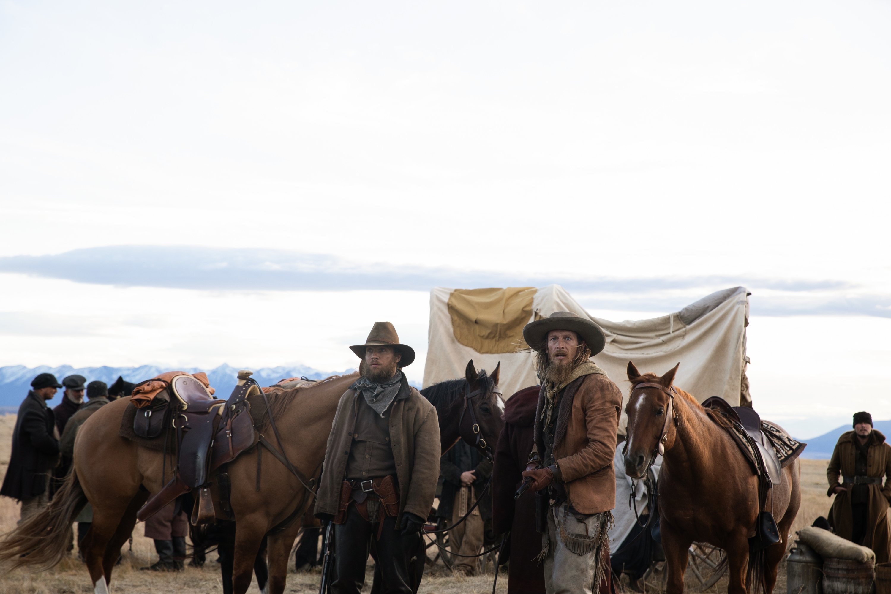 Noah le Gros as Colton and James Landry Hébert as Wade in 1883 Episode 9. The cowboys stand in front of a group of immigrants.