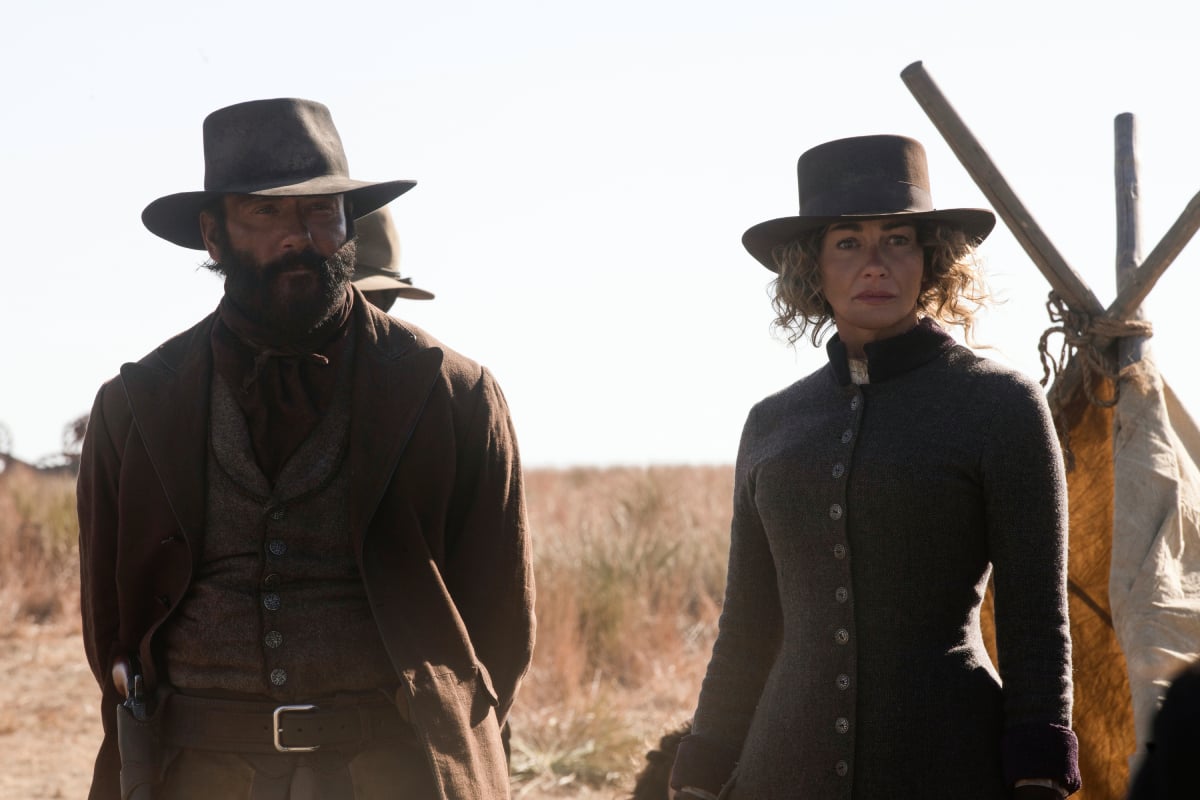 James and Faith Hill as Margaret of the Paramount+ original series 1883. James and Margaret stand in front of a tent.