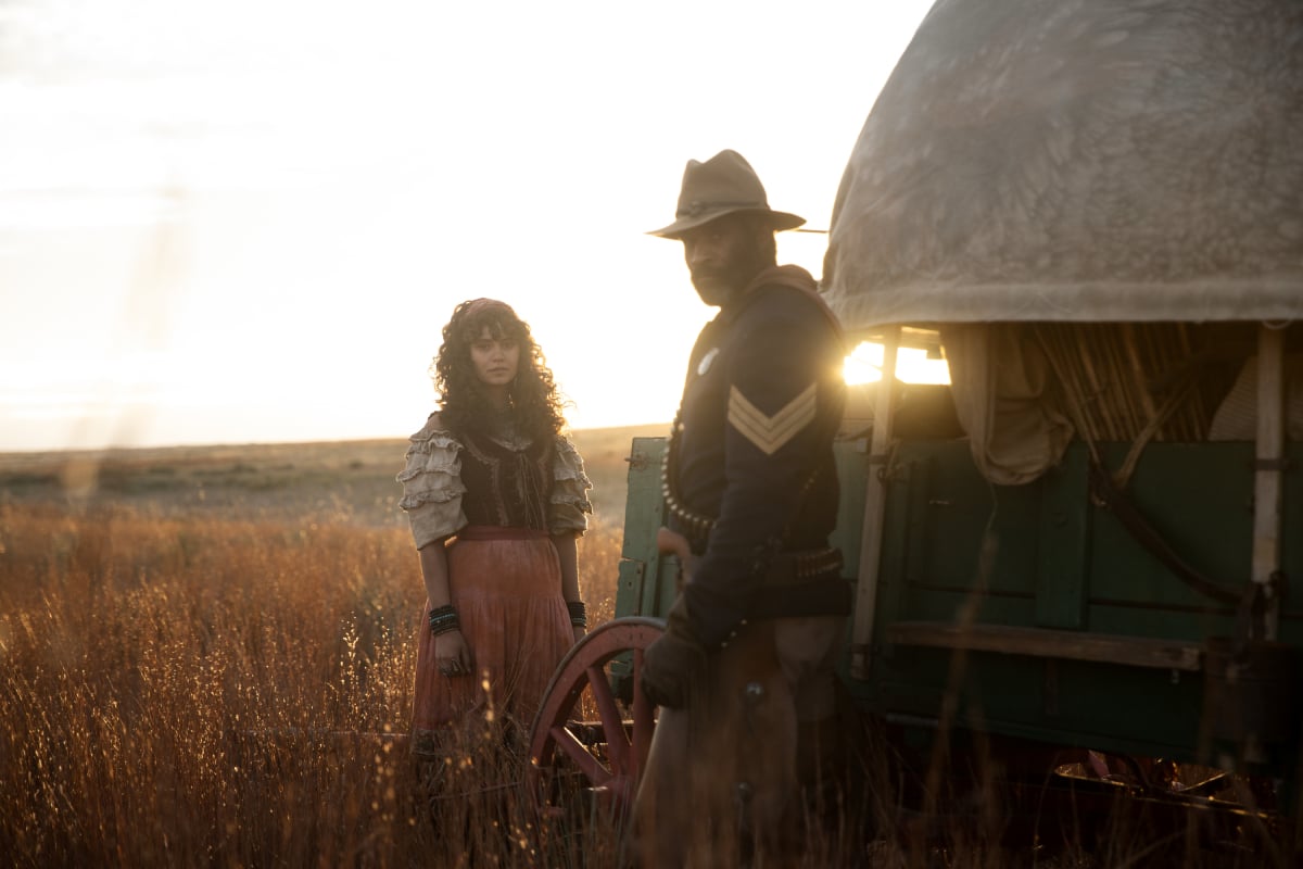 Gratiela Brancusi as Noemi and LaMonica Garrett as Thomas of the Paramount+ original series 1883. Thomas and Noemi stand beside a wagon.