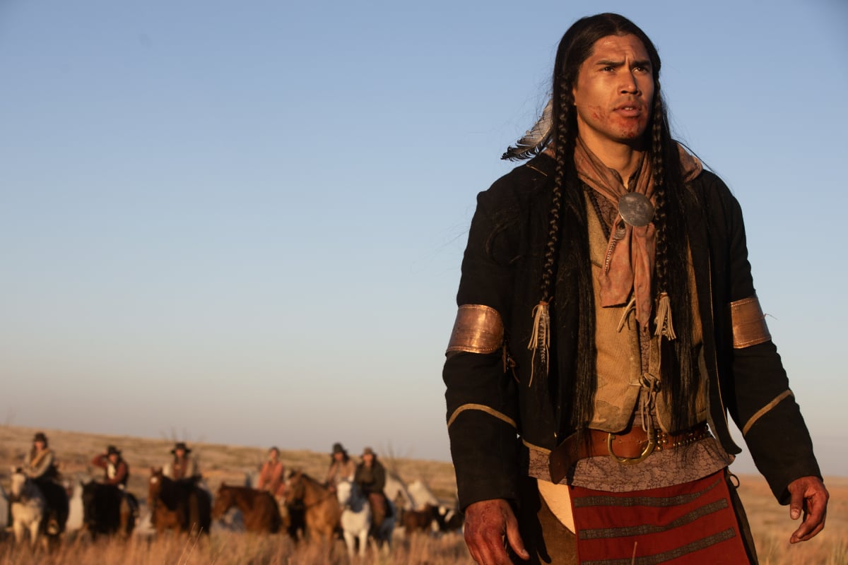 Martin Sensmeier as Sam in '1883' Episode 8. Sam stands in front of a group of people on horses.