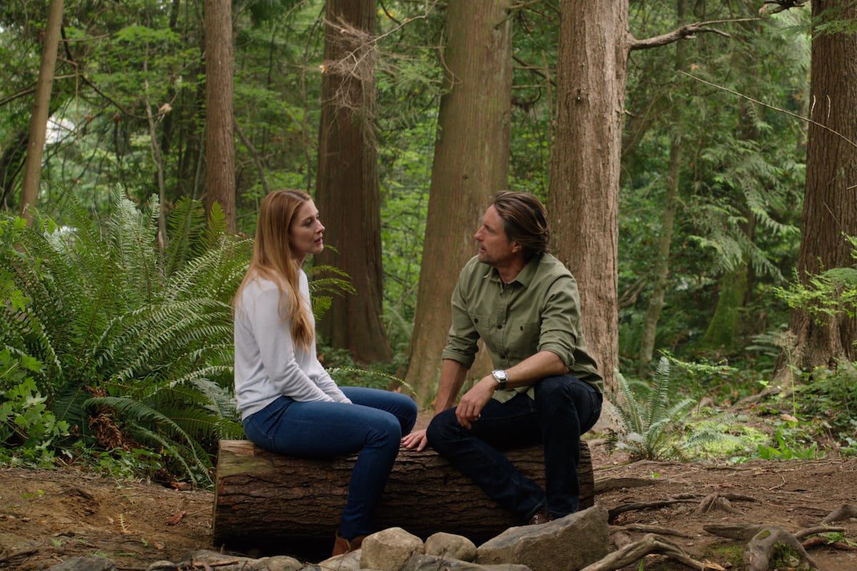 Alexandra Breckenridge as Mel Monore and Martin Henderson as Jack Sheridan sitting on a log in the woods in 'Virgin River'
