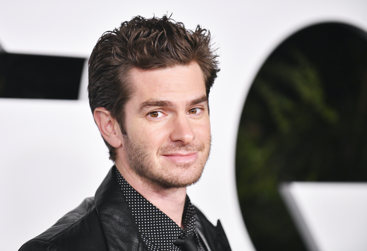 Andrew Garfield wears a dark suit and smiles on the red carpet