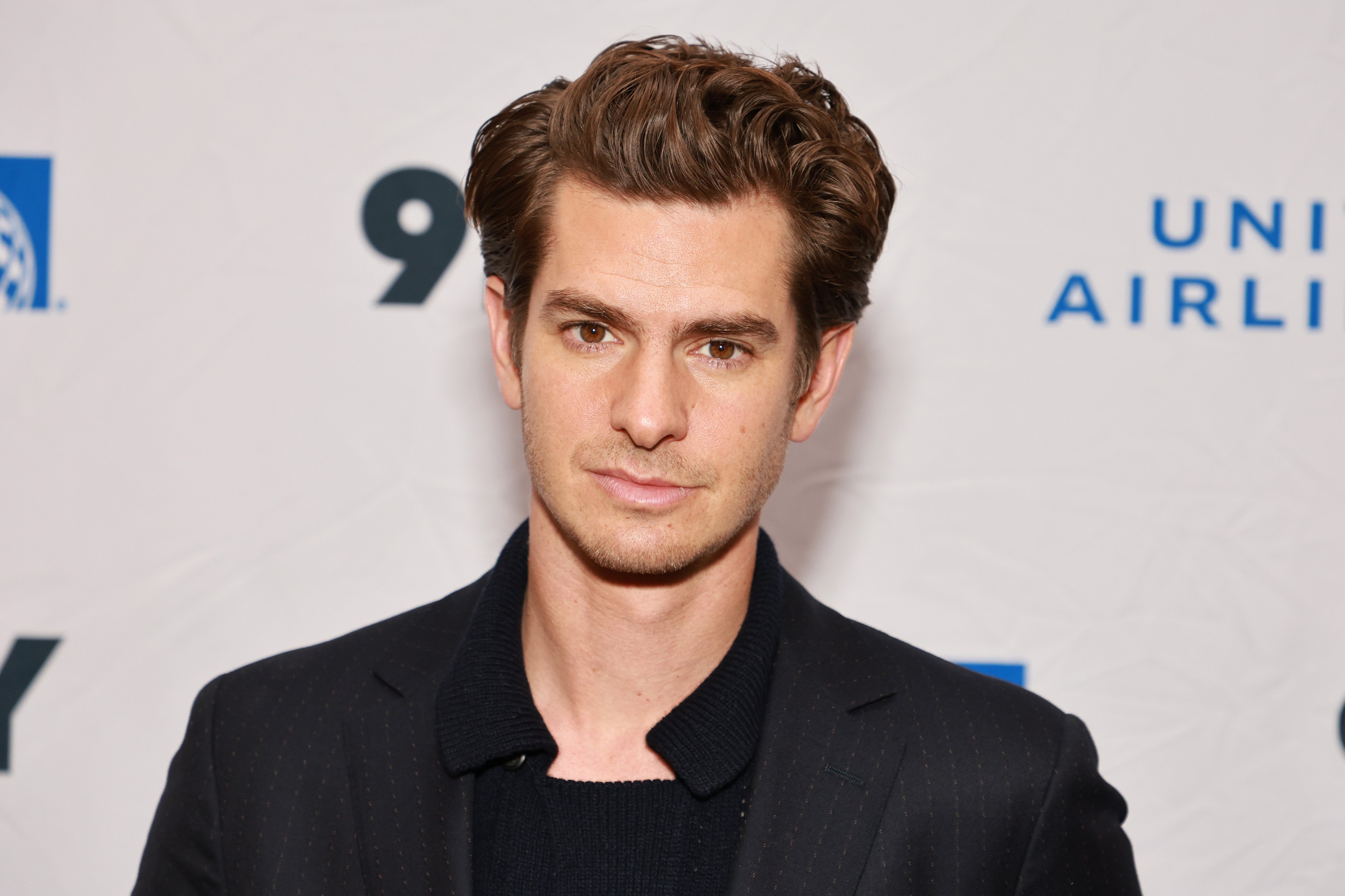 'Spider-Man: No Way Home' star Andrew Garfield wears a black suit jacket over a black sweater.