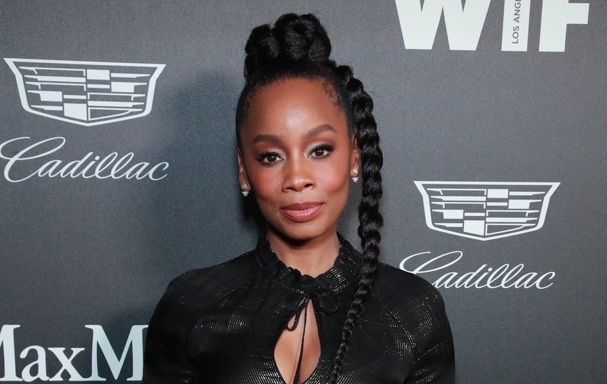 Anika Noni Rose wears a black dress with red lipstick at a media event